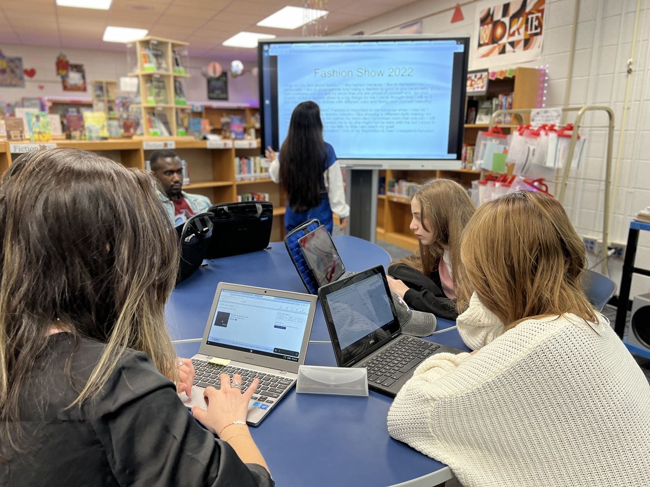 Students collaborating on laptops while one student presents on a SMART Board in the classroom.