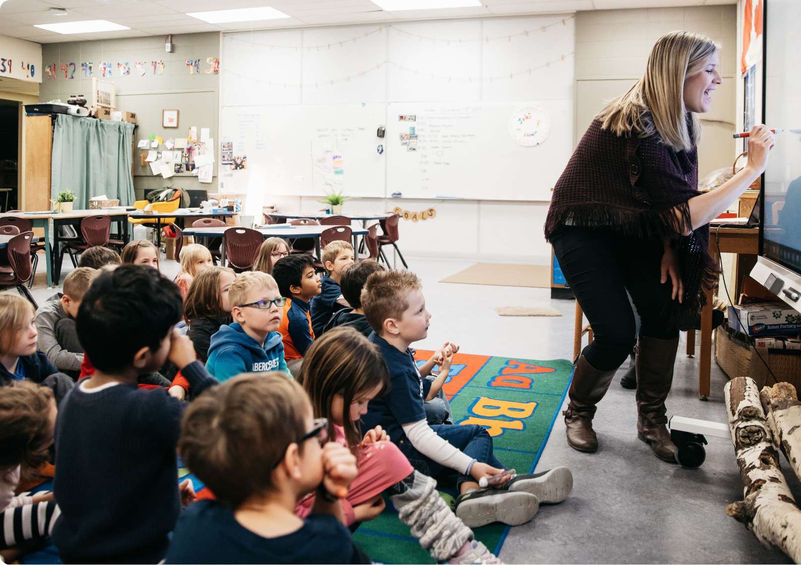 Teacher engaging with a classroom of young students seated on the floor looking towards her.