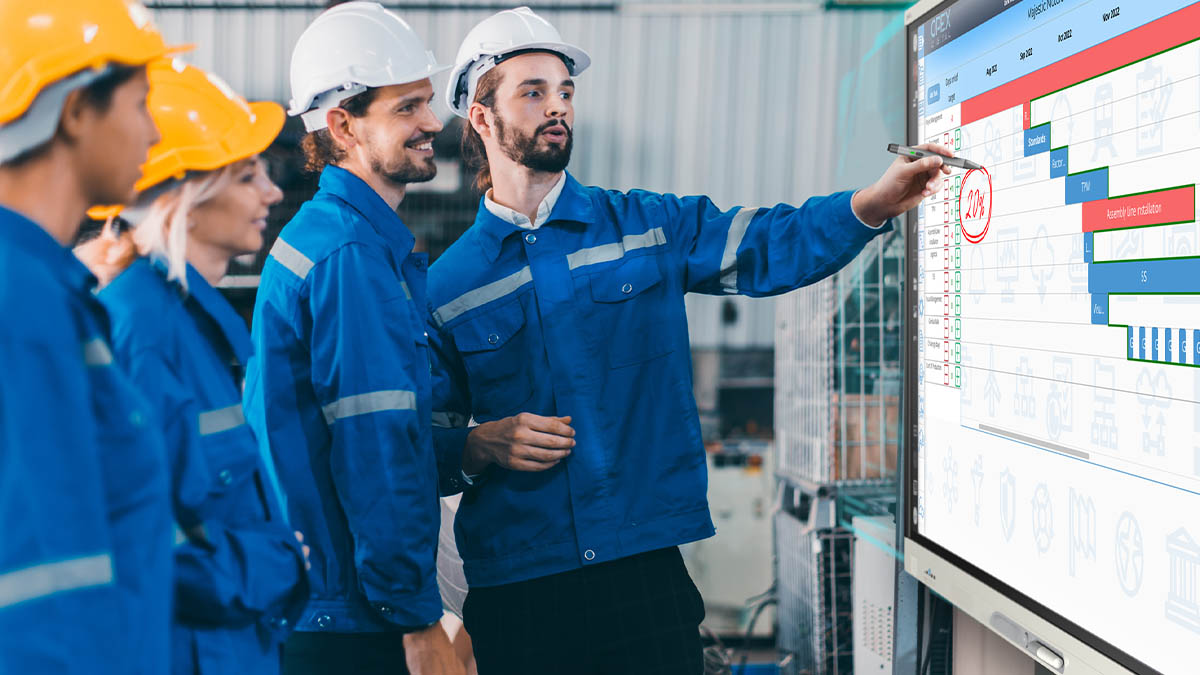 Team of engineers discussing production metrics on a SMART Board in a factory setting.